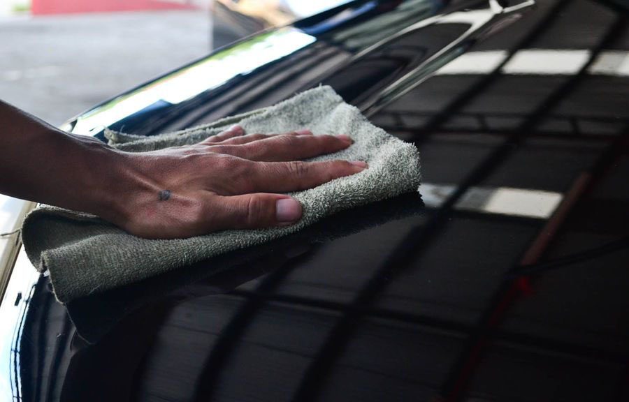 A hand polishing a car's glossy black paint with a microfiber cloth